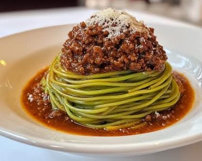 Spaghetti verts à la bolognaise, nappés de sauce tomate et garnis de parmesan râpé.