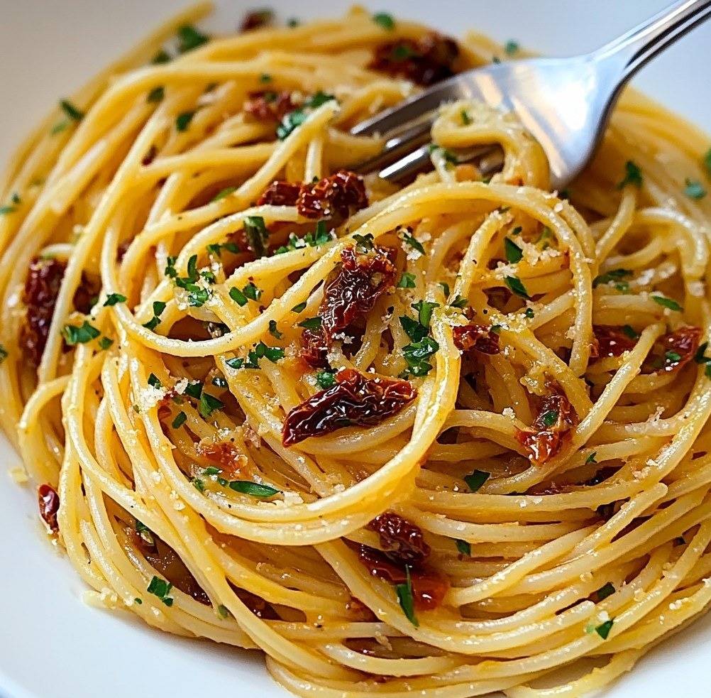 Assiette de spaghetti aux tomates séchées et à l’huile d’olive à l’ail, garnie de persil frais et de parmesan râpé.