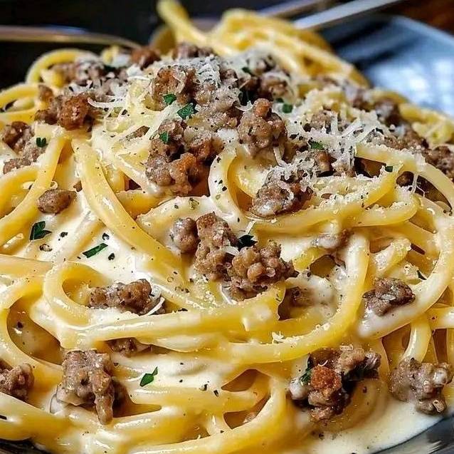 Assiette de linguine crémeux à l’ail et au fromage, garnie de persil frais et de viande hachée dorée.