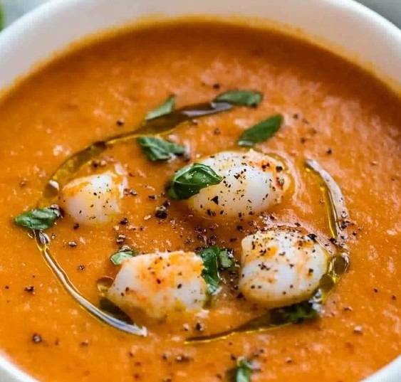 Bol de soupe tomate-basilic crémeuse, garnie de crevettes poêlées et de feuilles de basilic frais.