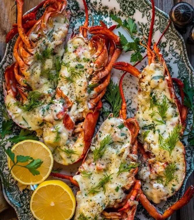 Gambas grillées dorées servies avec du beurre fondu, ail, persil et citron sur une assiette.