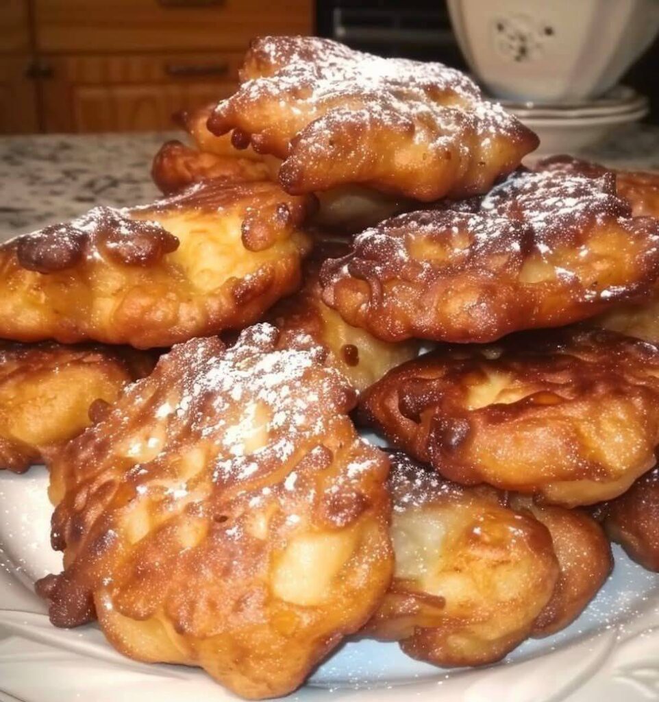 Beignets dorés aux pommes, saupoudrés de sucre glace, servis sur une assiette avec une tasse de thé.