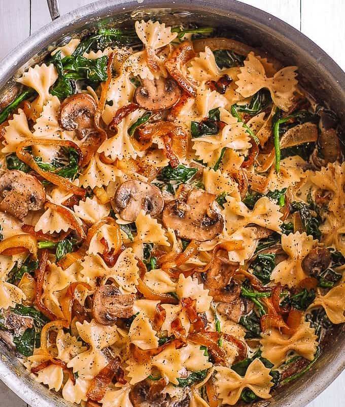 Assiette de farfalle nappées de sauce crémeuse aux champignons et épinards, garnies d’oignons caramélisés et de parmesan râpé