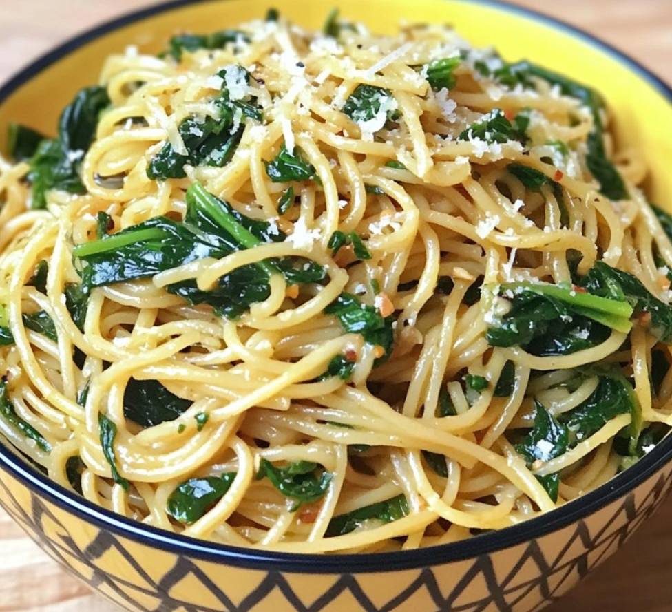 Un bol de nouilles sautées à l’ail et aux épinards, agrémenté de parmesan râpé et de flocons de piment.