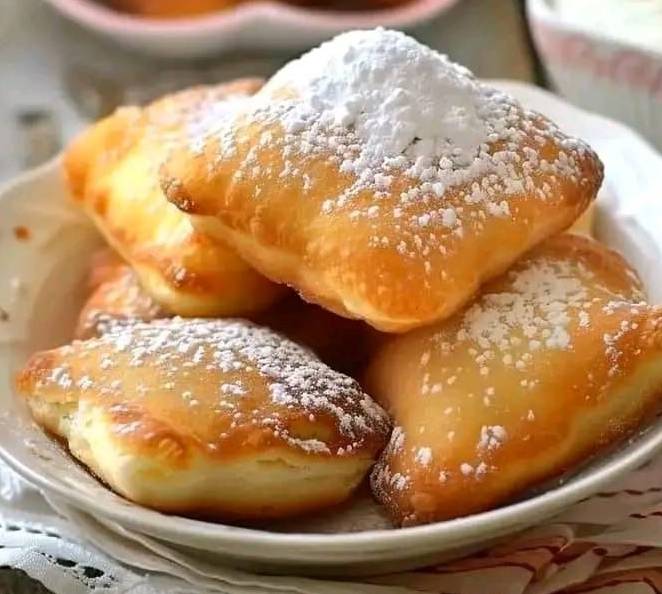 Beignets dorés et moelleux saupoudrés de sucre glace, servis sur une assiette.

